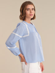 Woman wearing a light blue striped blouse with white trim on a beige background