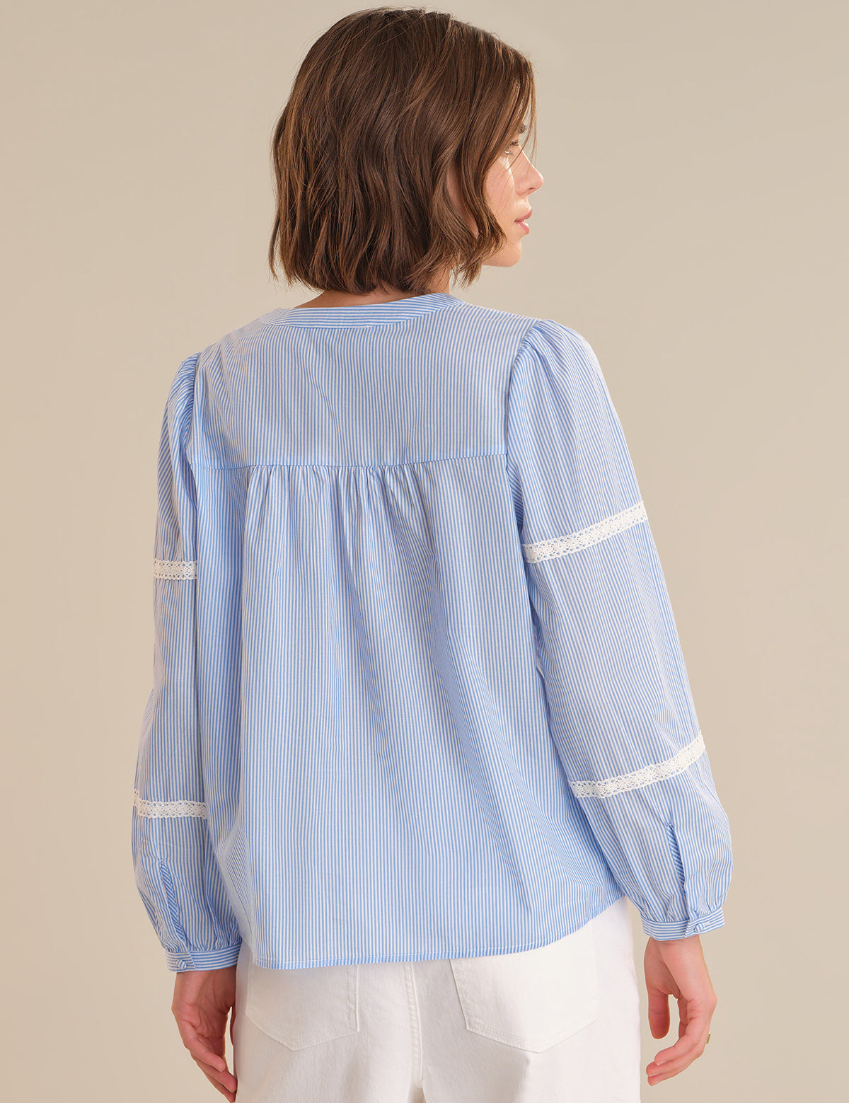 Woman wearing a light blue striped blouse with white trim on a beige background