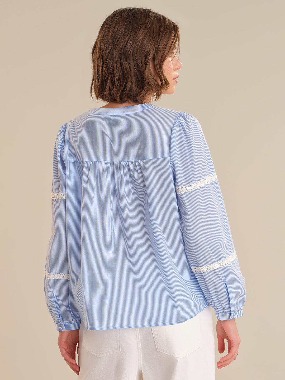 Woman wearing a light blue striped blouse with white trim on a beige background