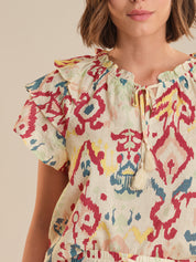 Woman wearing a colorful patterned blouse with tassels on a neutral background
