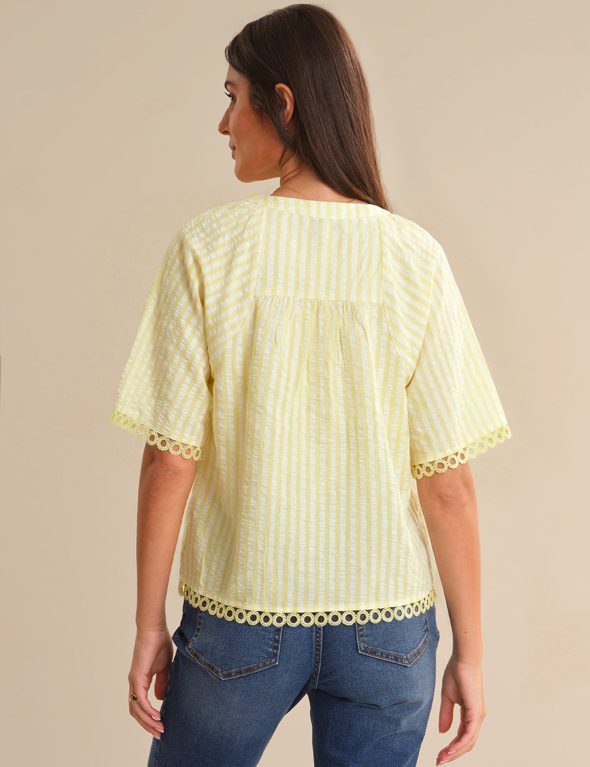 Woman wearing a light yellow blouse with lace trim on a beige background