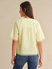 Woman wearing a light yellow blouse with lace trim on a beige background