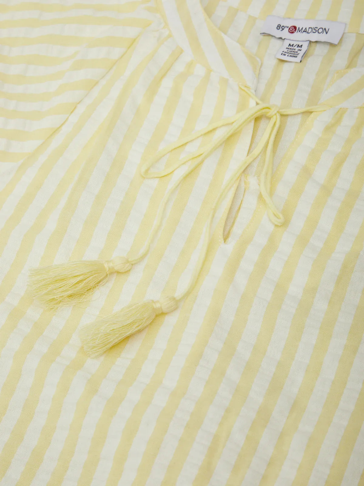 Yellow and white striped fabric with tassels and a visible brand label.