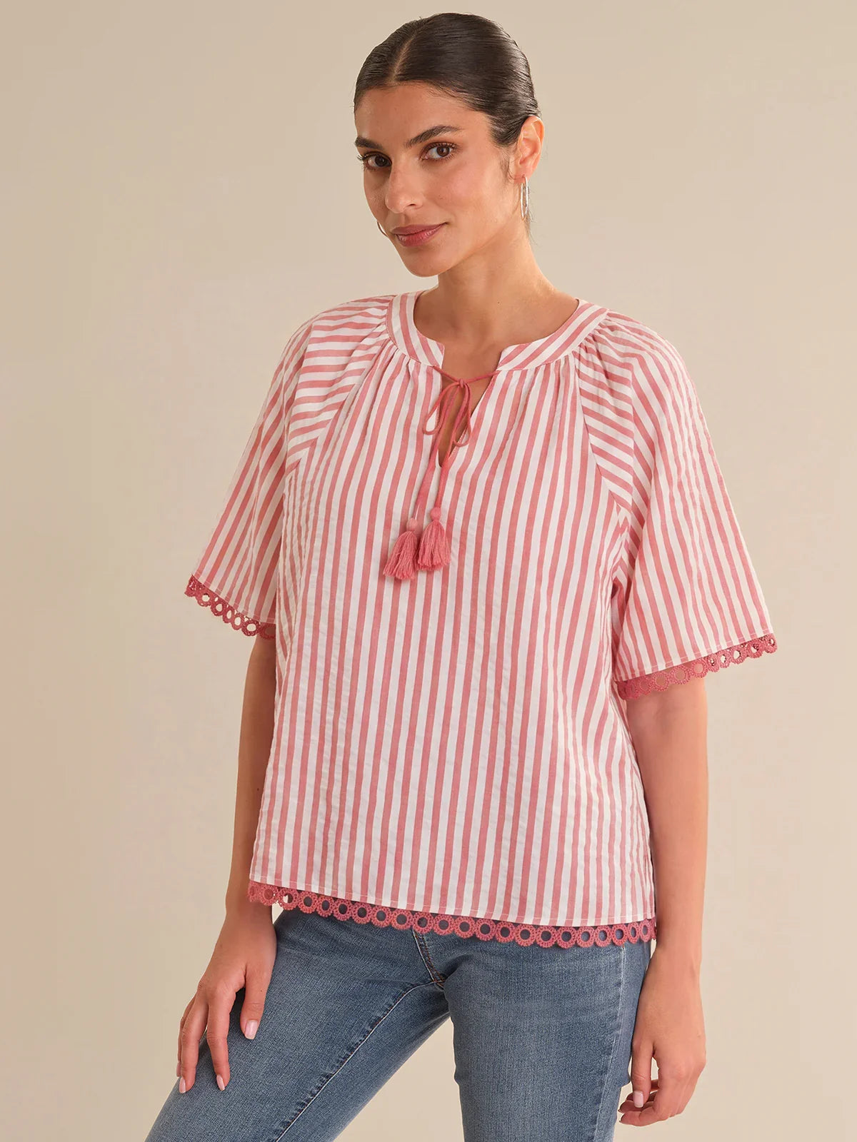 Woman wearing a red and white striped blouse with tassels on a beige background