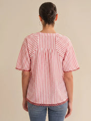 Person wearing a red and white striped shirt with scalloped hem on a beige background