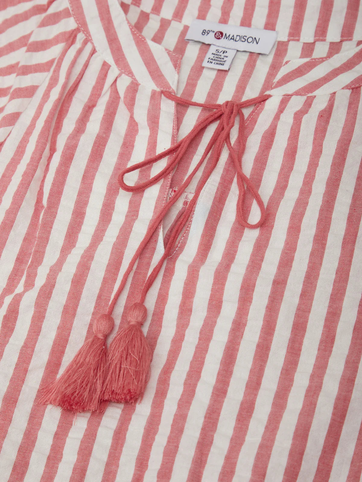 Red and white striped shirt with a tassel and brand label on a matching background