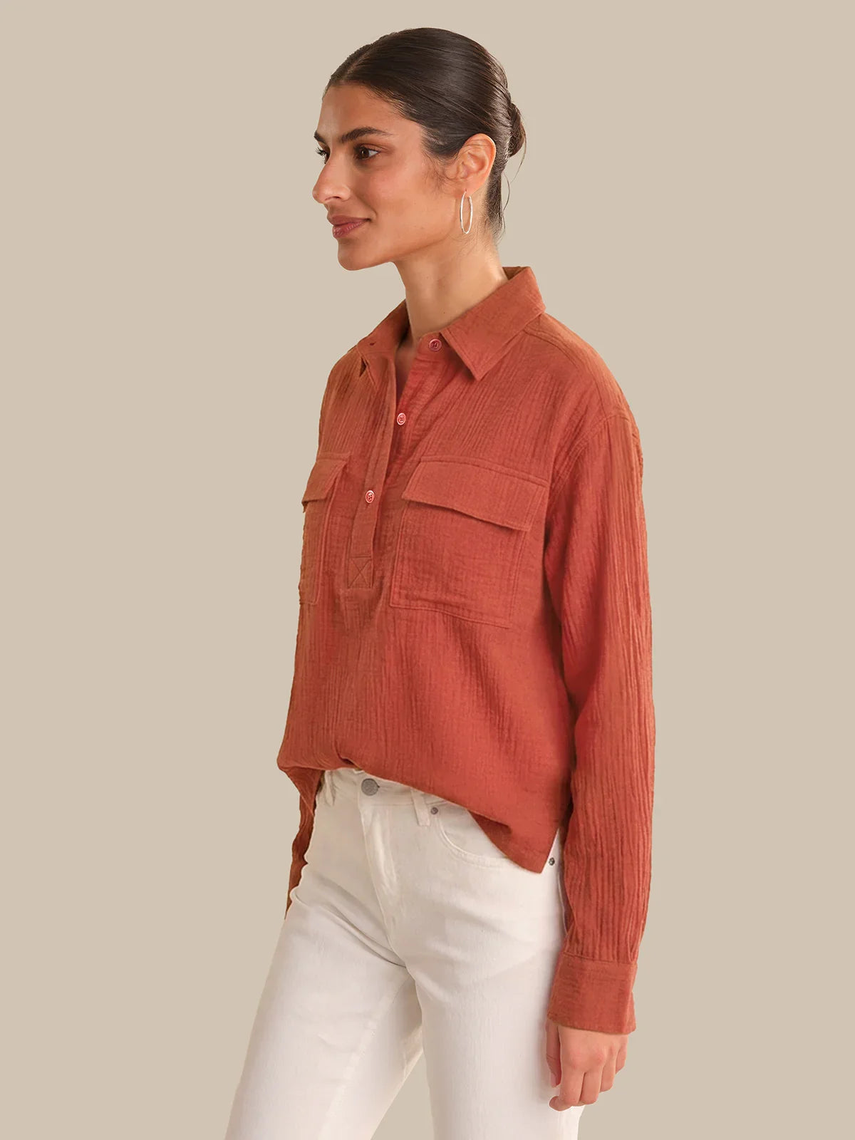 Woman wearing a rust-colored corduroy shirt and white pants on a beige background