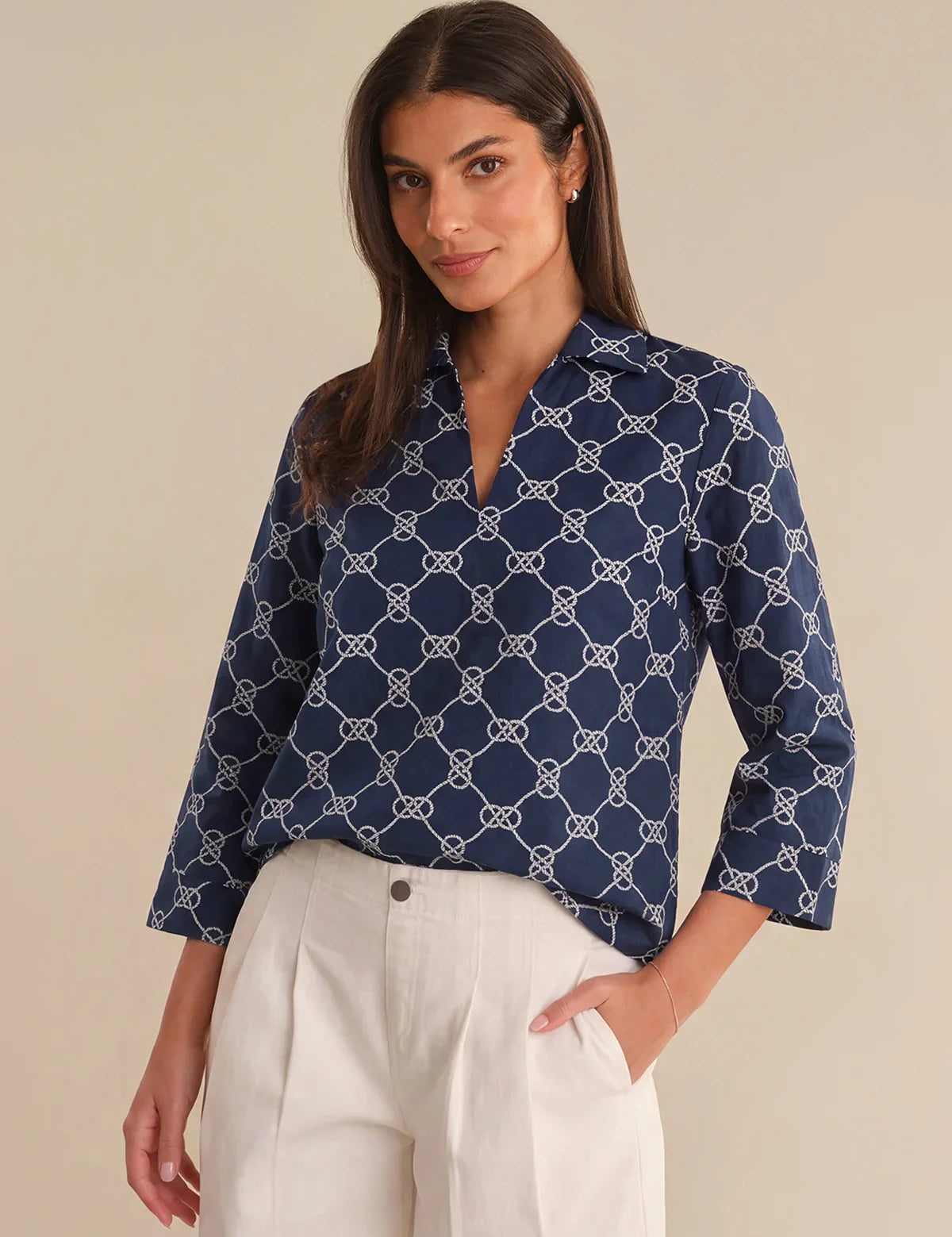 Woman wearing a navy blue patterned blouse with white pants on a beige background