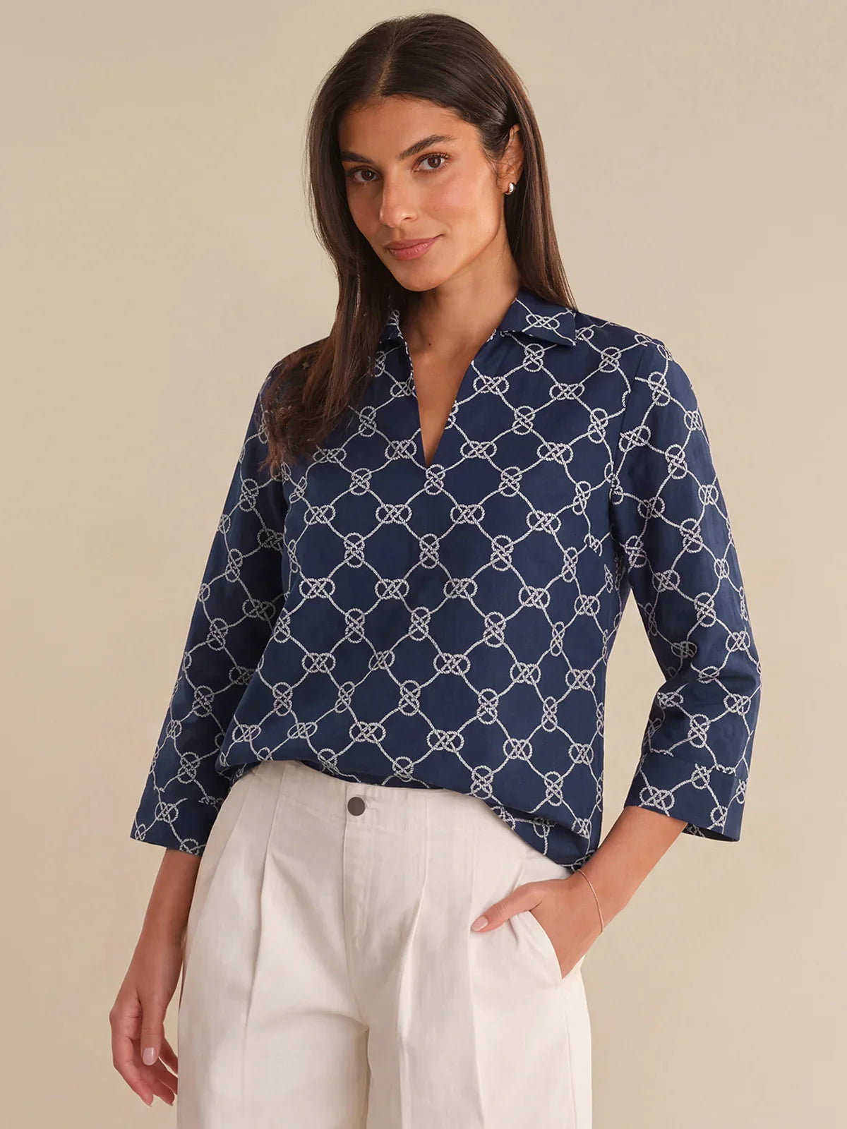 Woman wearing a navy blue patterned blouse with white pants on a beige background