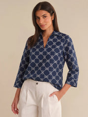 Woman wearing a navy blue patterned blouse with white pants on a beige background