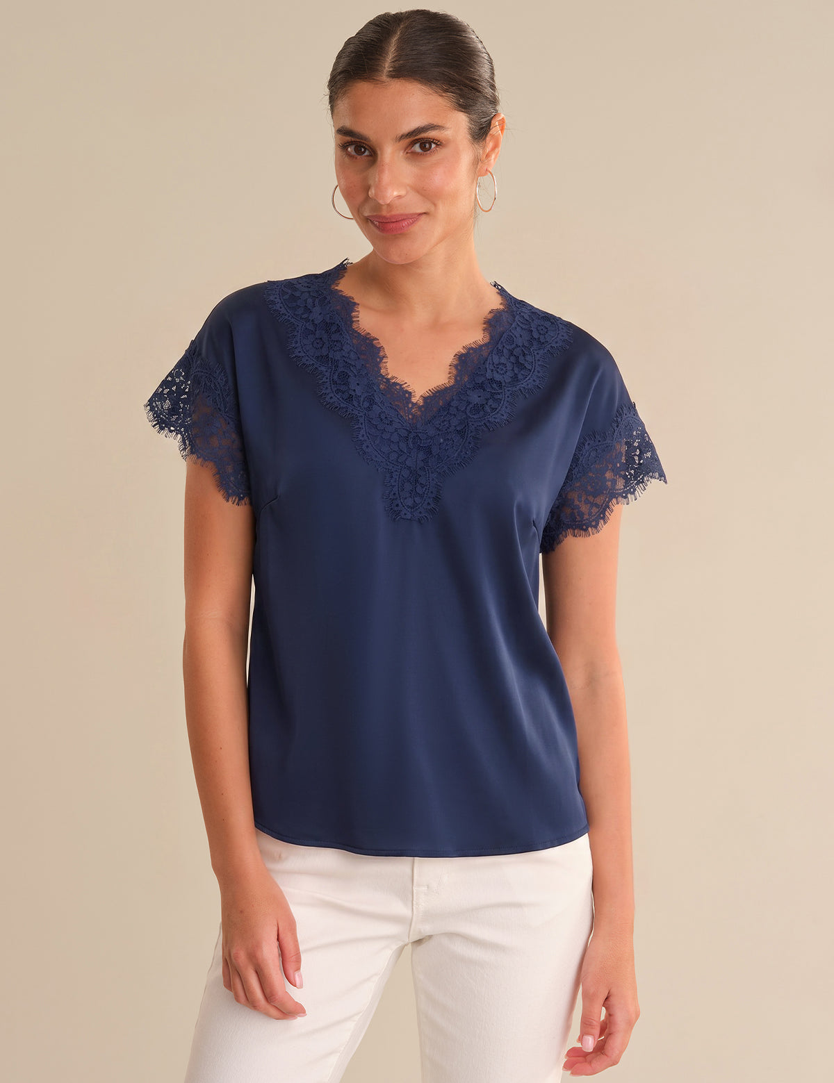 Woman wearing a navy blue blouse with lace sleeves on a beige background