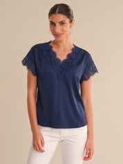 Woman wearing a navy blue blouse with lace sleeves on a beige background