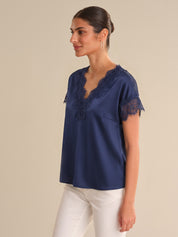 Woman wearing a navy blue blouse with lace details on a beige background