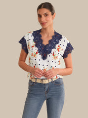 Woman wearing a white blouse with blue lace details and floral patterns, paired with blue jeans on a beige background.