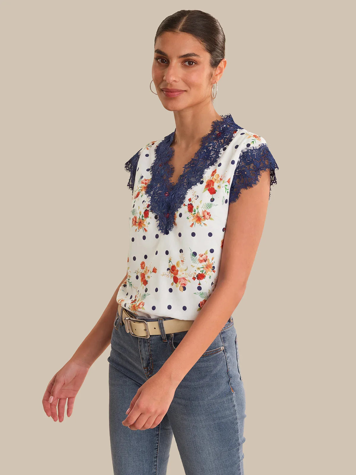 Woman wearing a floral blouse with lace details and jeans on a beige background