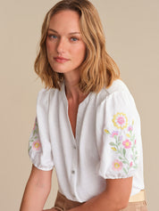 Woman wearing a white blouse with floral embroidery on a beige background