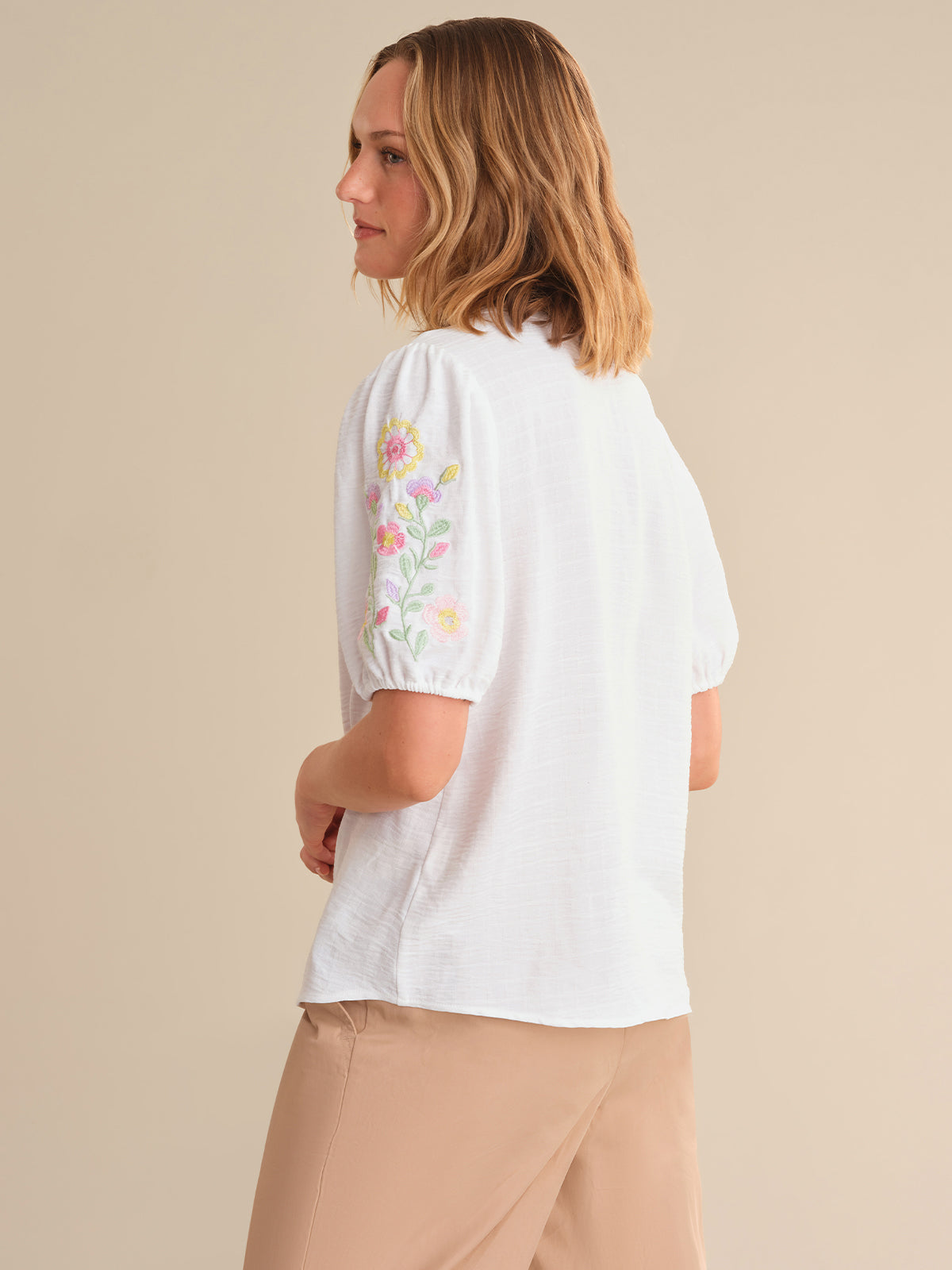 Woman wearing a white blouse with floral embroidery on a beige background