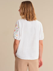 Woman wearing a white blouse with floral sleeve designs on a beige background