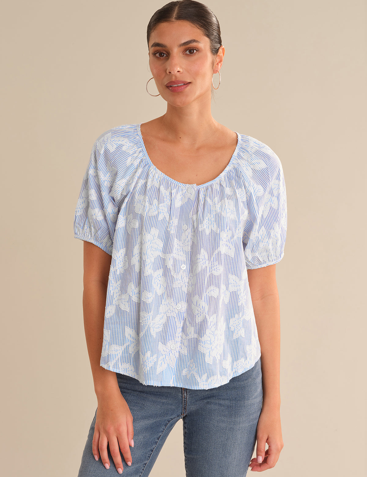 Woman wearing a light blue patterned top and jeans against a beige background