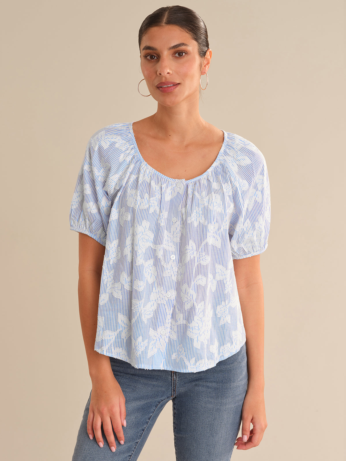 Woman wearing a light blue patterned top and jeans against a beige background