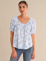 Woman wearing a light blue patterned top and jeans against a beige background