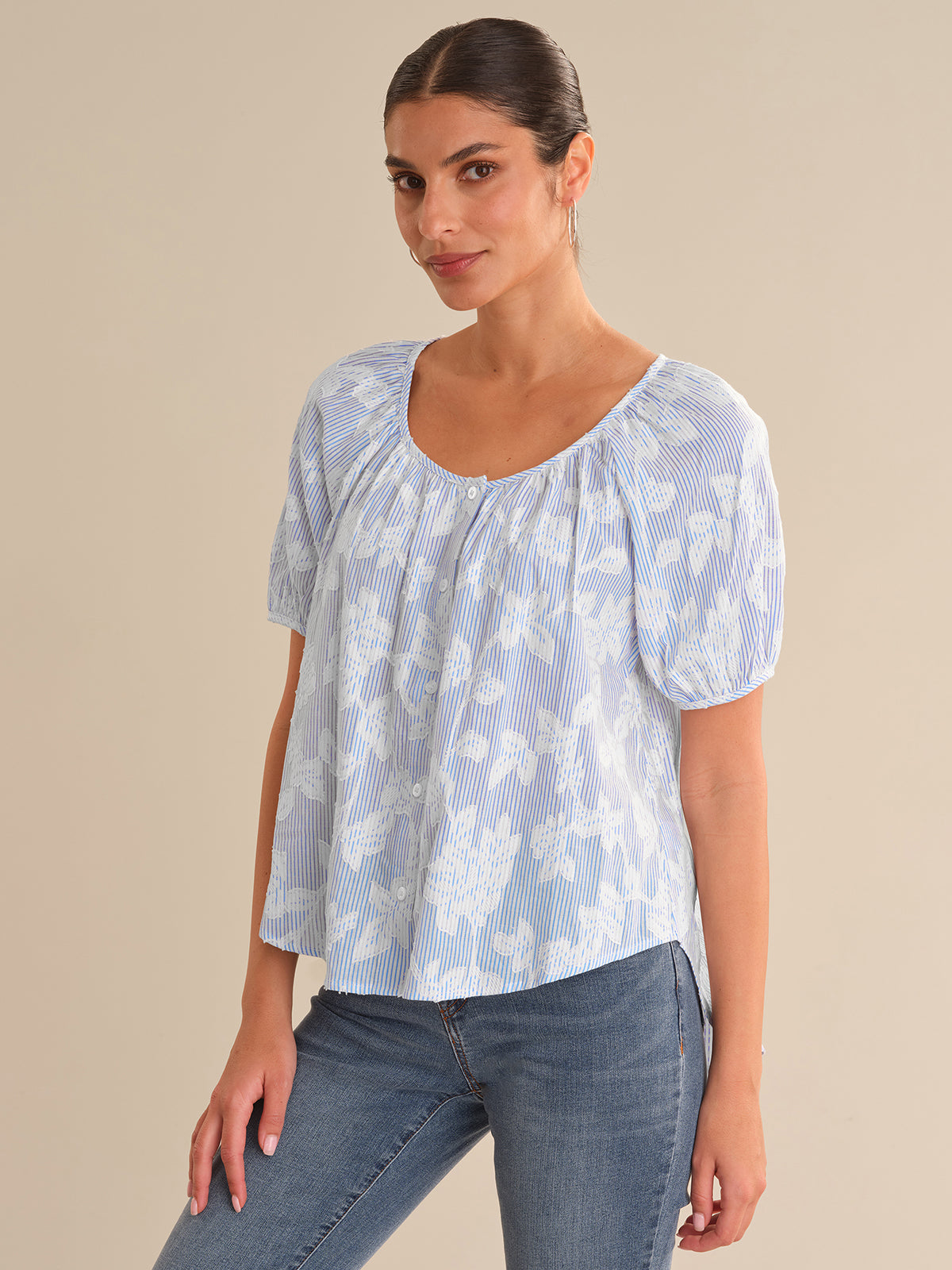 Woman wearing a light blue floral blouse and jeans on a beige background