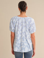 Person wearing a light blue floral blouse against a beige background