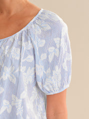 Close-up of a blue and white striped shirt with floral patterns on a beige background