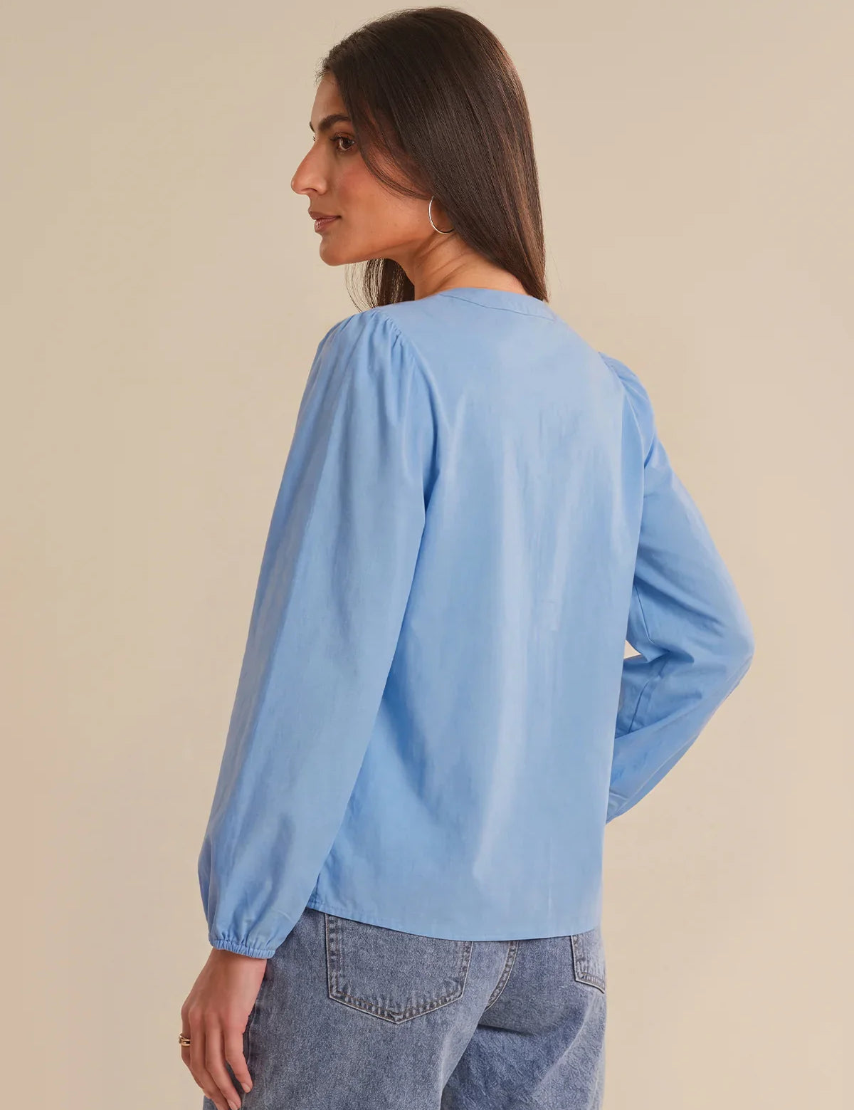 Woman wearing a light blue blouse with long sleeves on a beige background