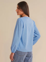 Woman wearing a light blue blouse with long sleeves on a beige background