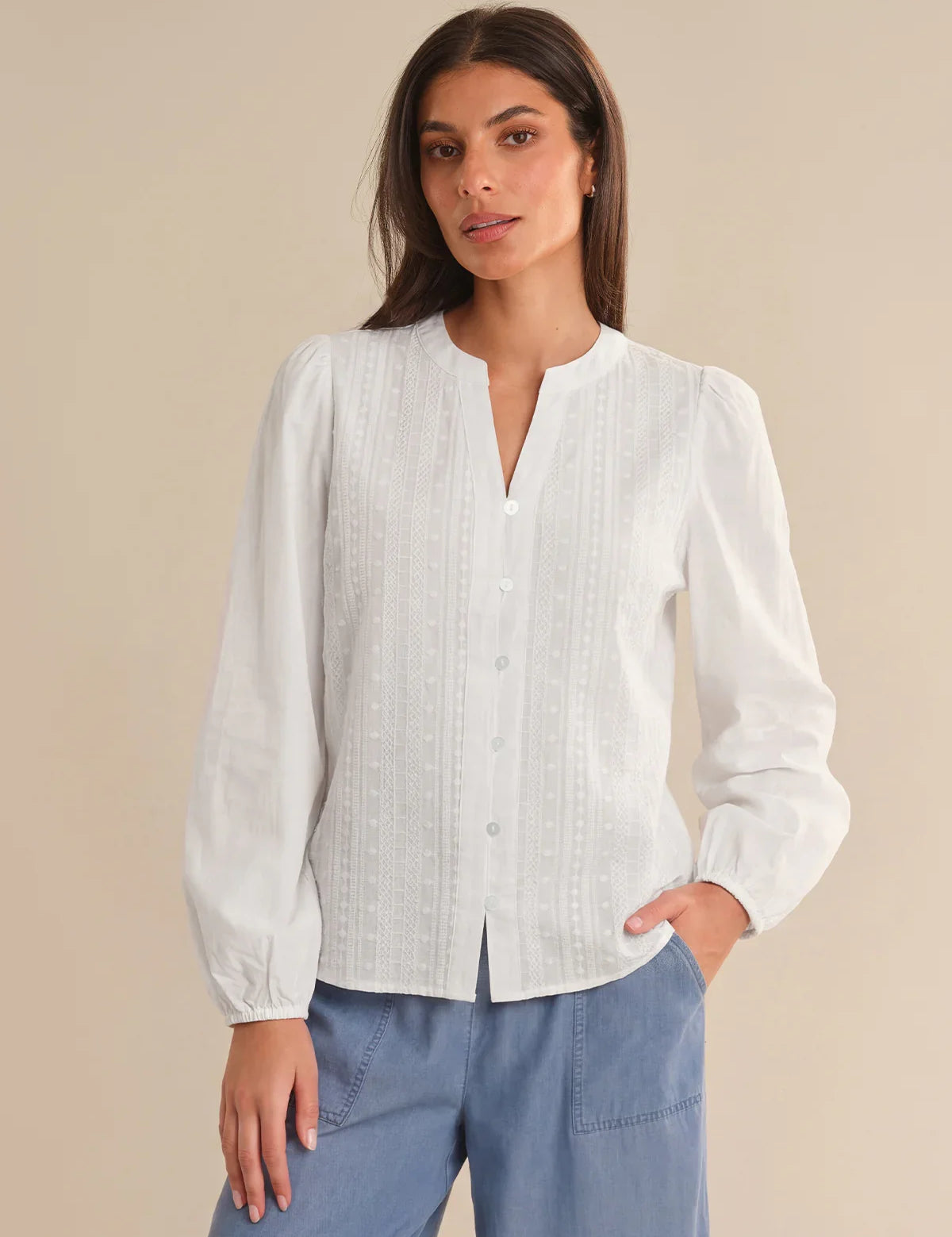 Woman wearing a white blouse with long sleeves against a beige background
