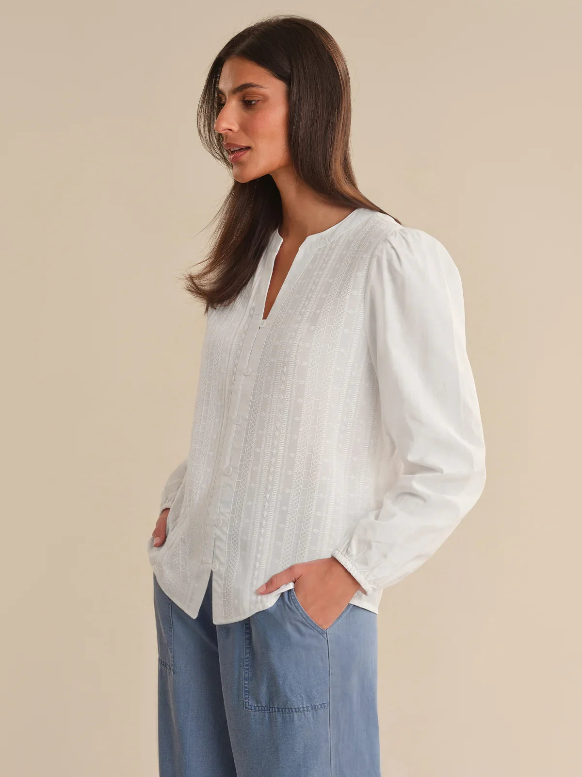 Woman wearing a white textured blouse and blue jeans against a beige background