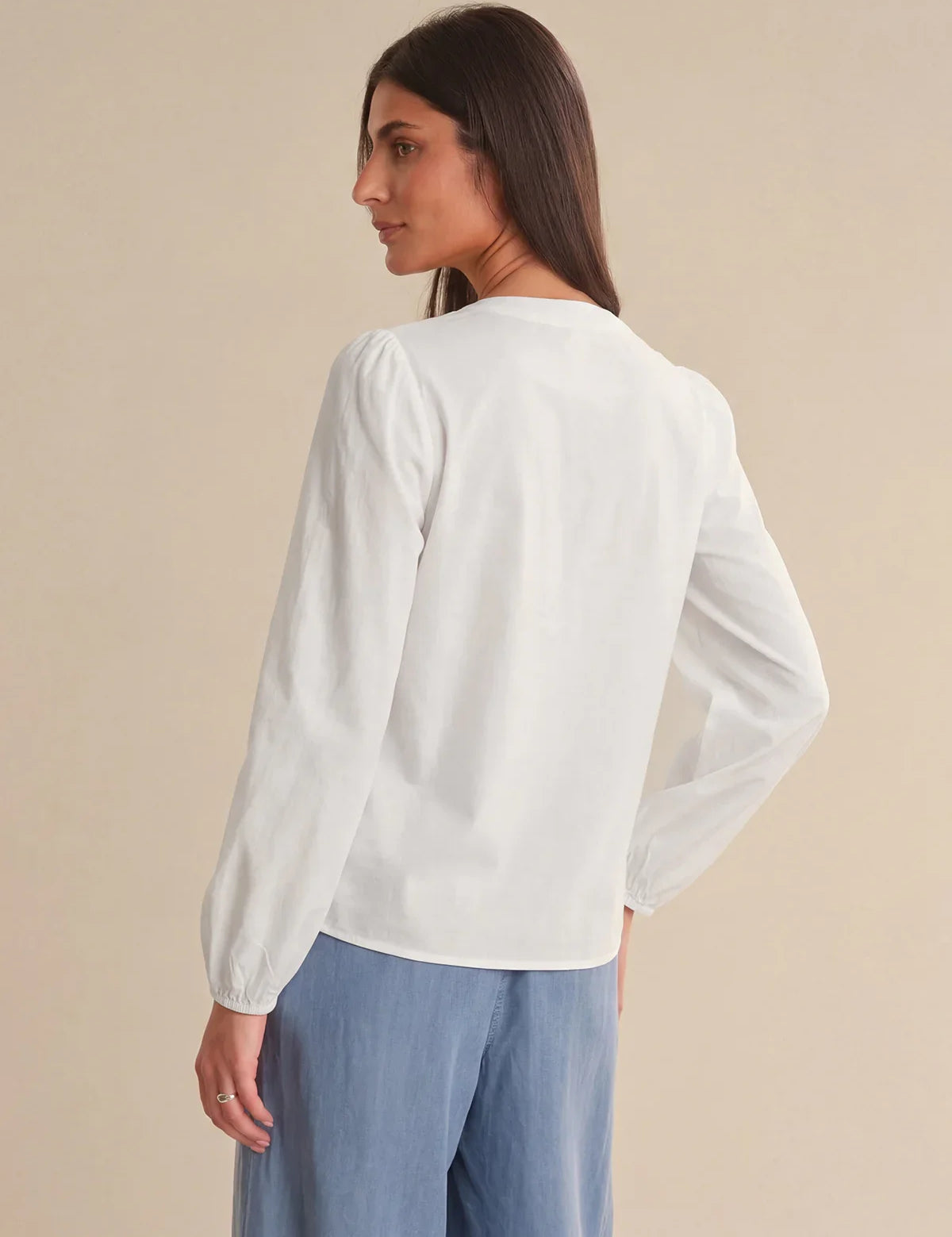 Woman wearing a white blouse and blue pants against a beige background