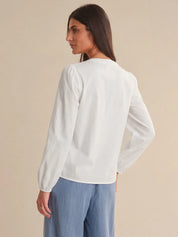 Woman wearing a white blouse and blue pants against a beige background