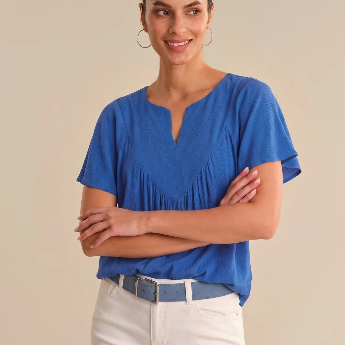 Woman wearing a blue blouse and white pants against a beige background