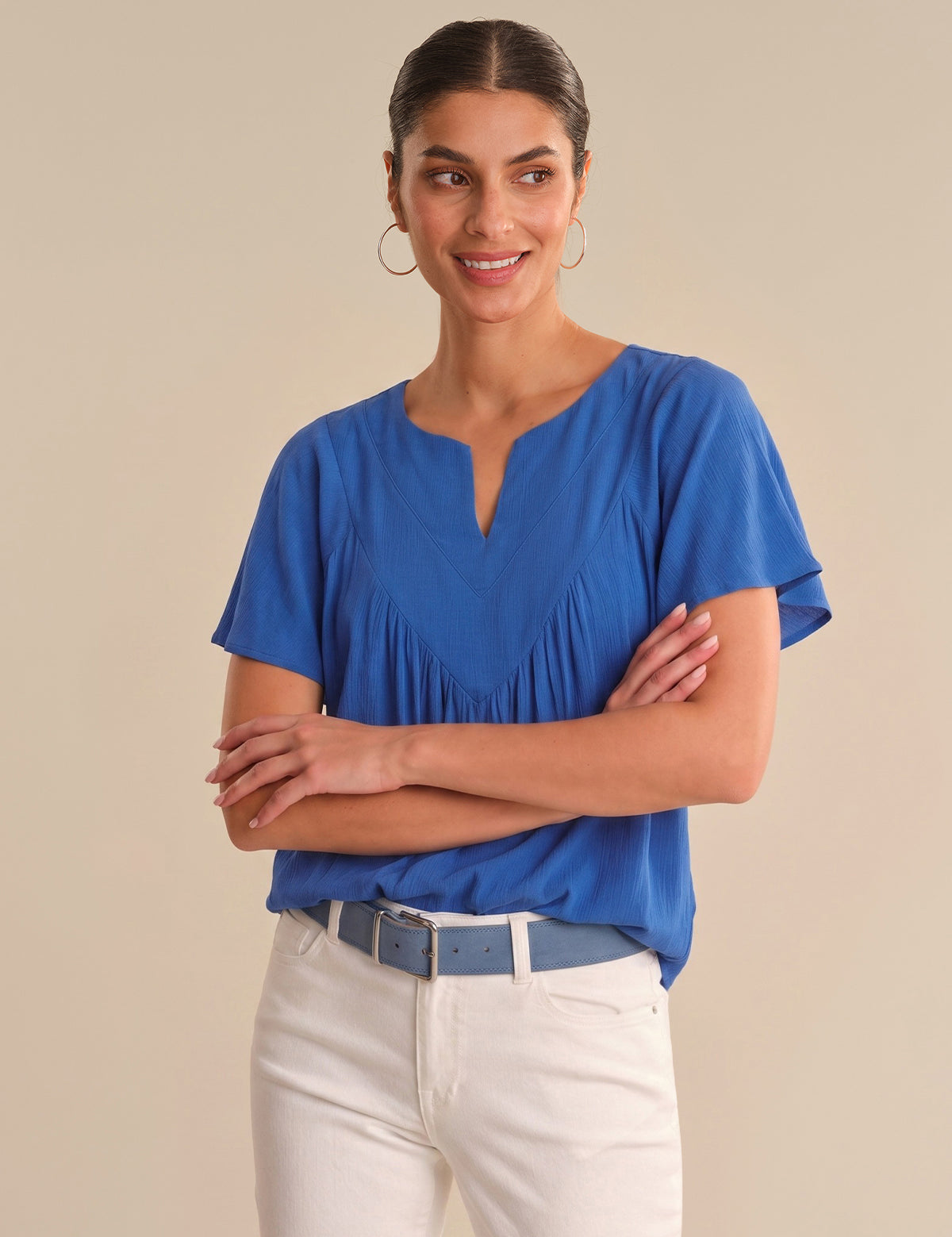 Woman wearing a blue blouse and white pants against a beige background