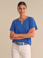 Woman wearing a blue blouse and white pants against a beige background