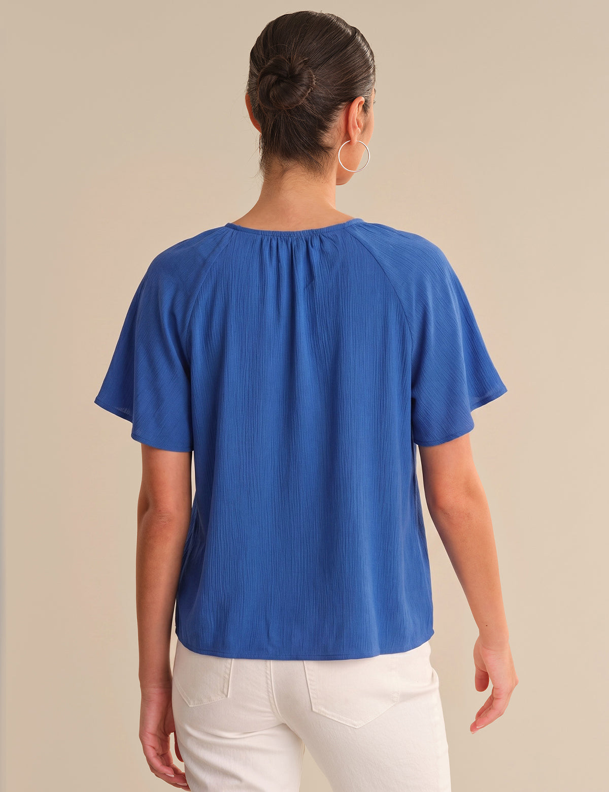 Person wearing a blue top and white pants on a beige background