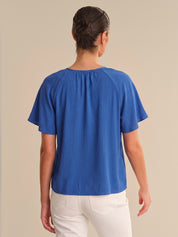 Person wearing a blue top and white pants on a beige background
