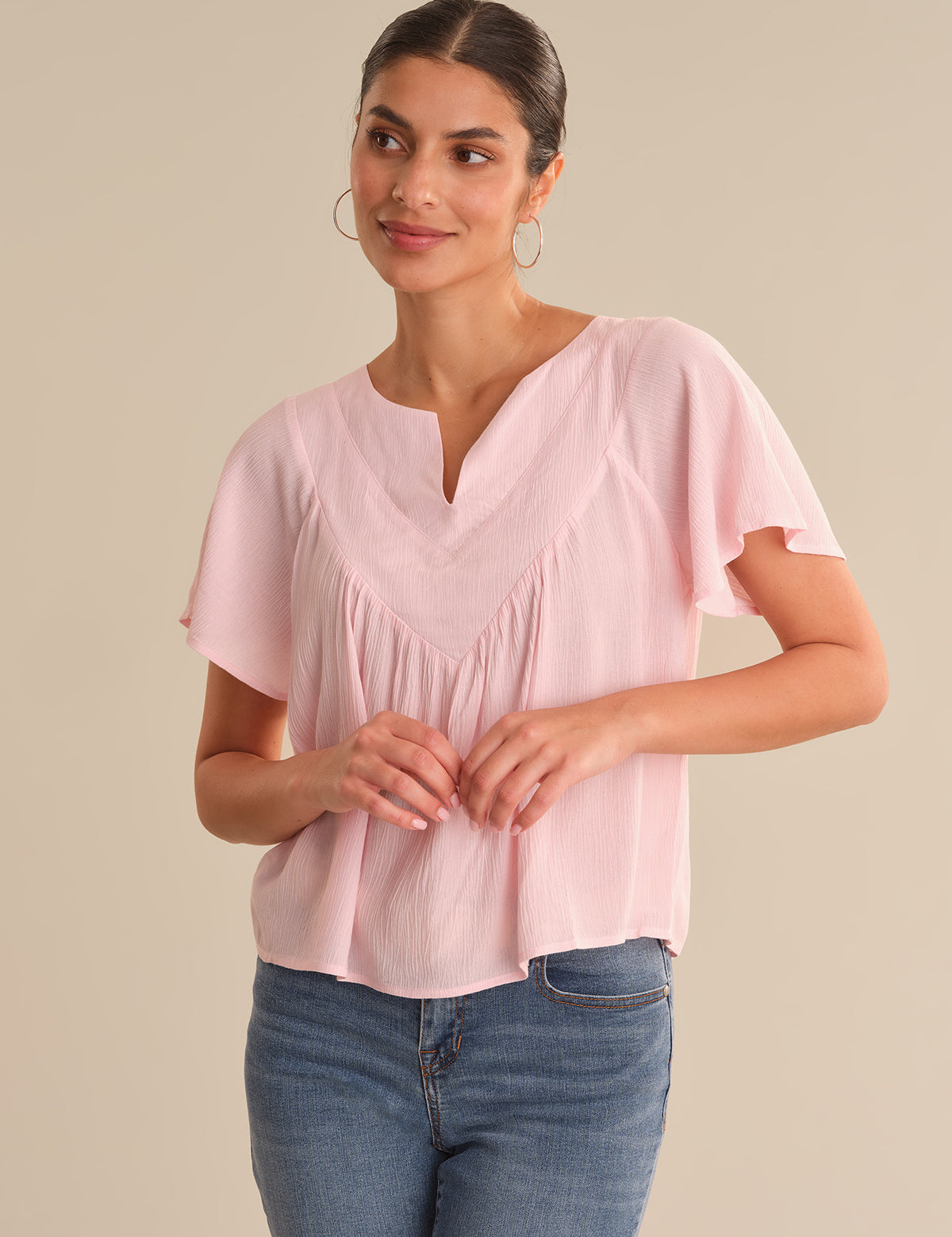 Woman wearing a pink blouse and blue jeans on a beige background