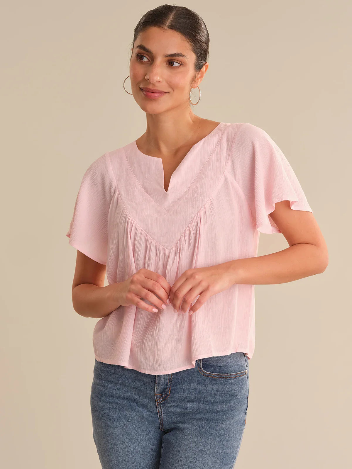 Woman wearing a pink blouse and blue jeans on a beige background