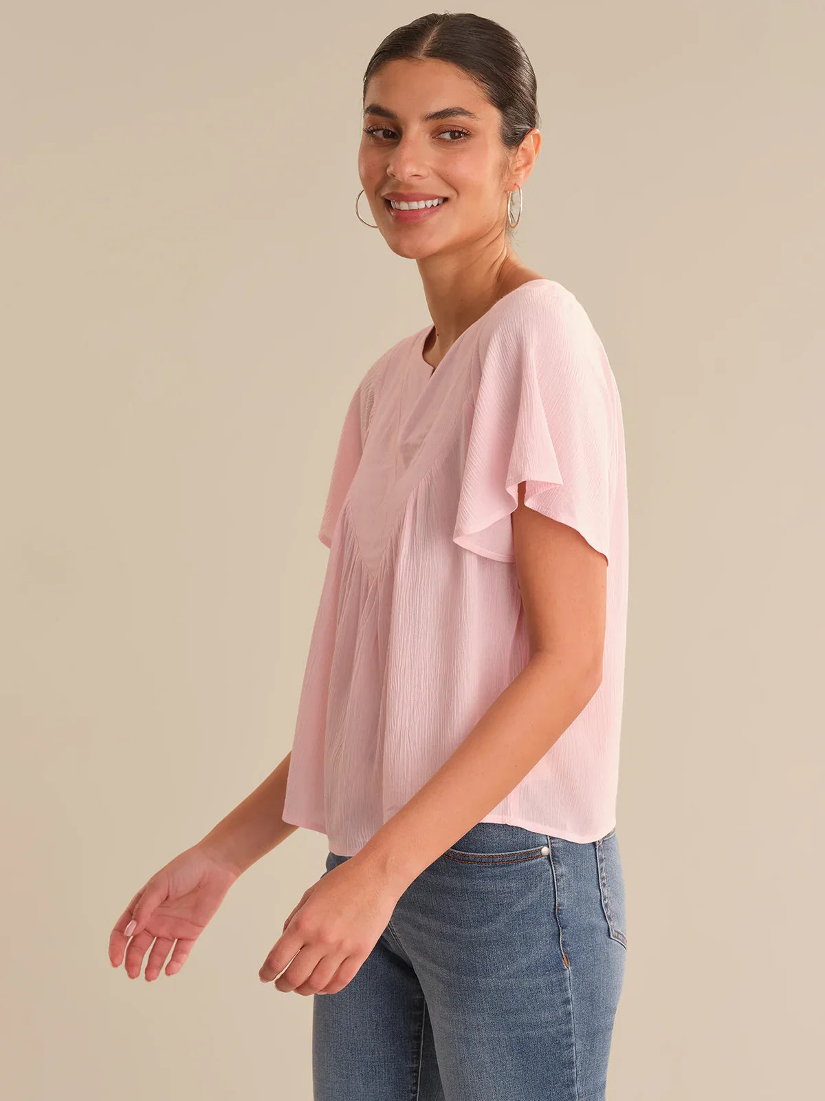 Woman wearing a light pink blouse and blue jeans against a beige background