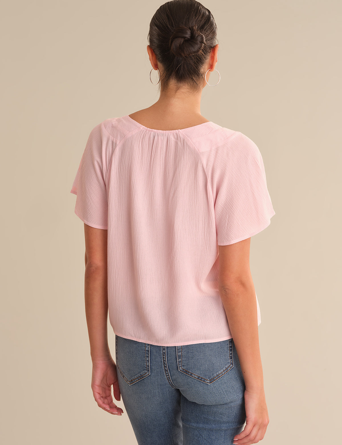 Person wearing a light pink blouse and blue jeans on a beige background