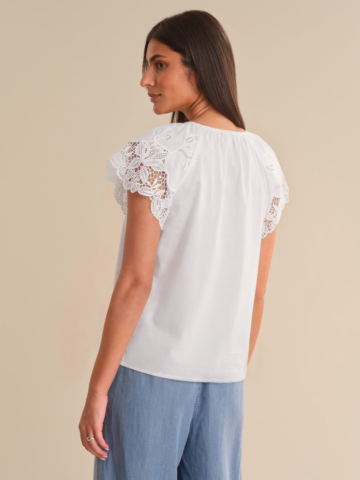 Woman wearing a white blouse with lace sleeves on a beige background