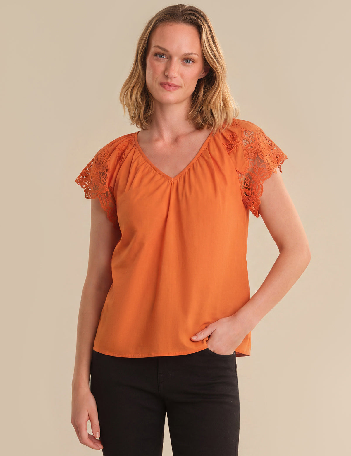 Woman wearing an orange blouse with lace sleeves against a beige background