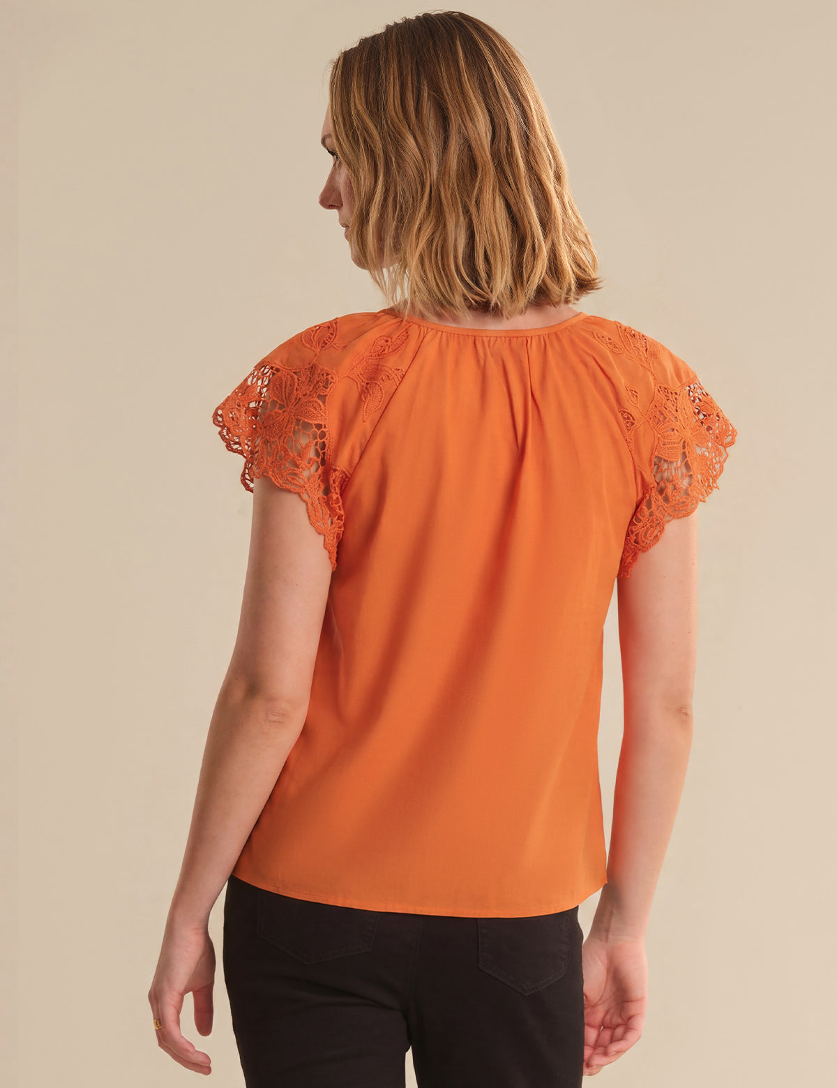 Woman wearing an orange blouse with lace sleeves against a beige background