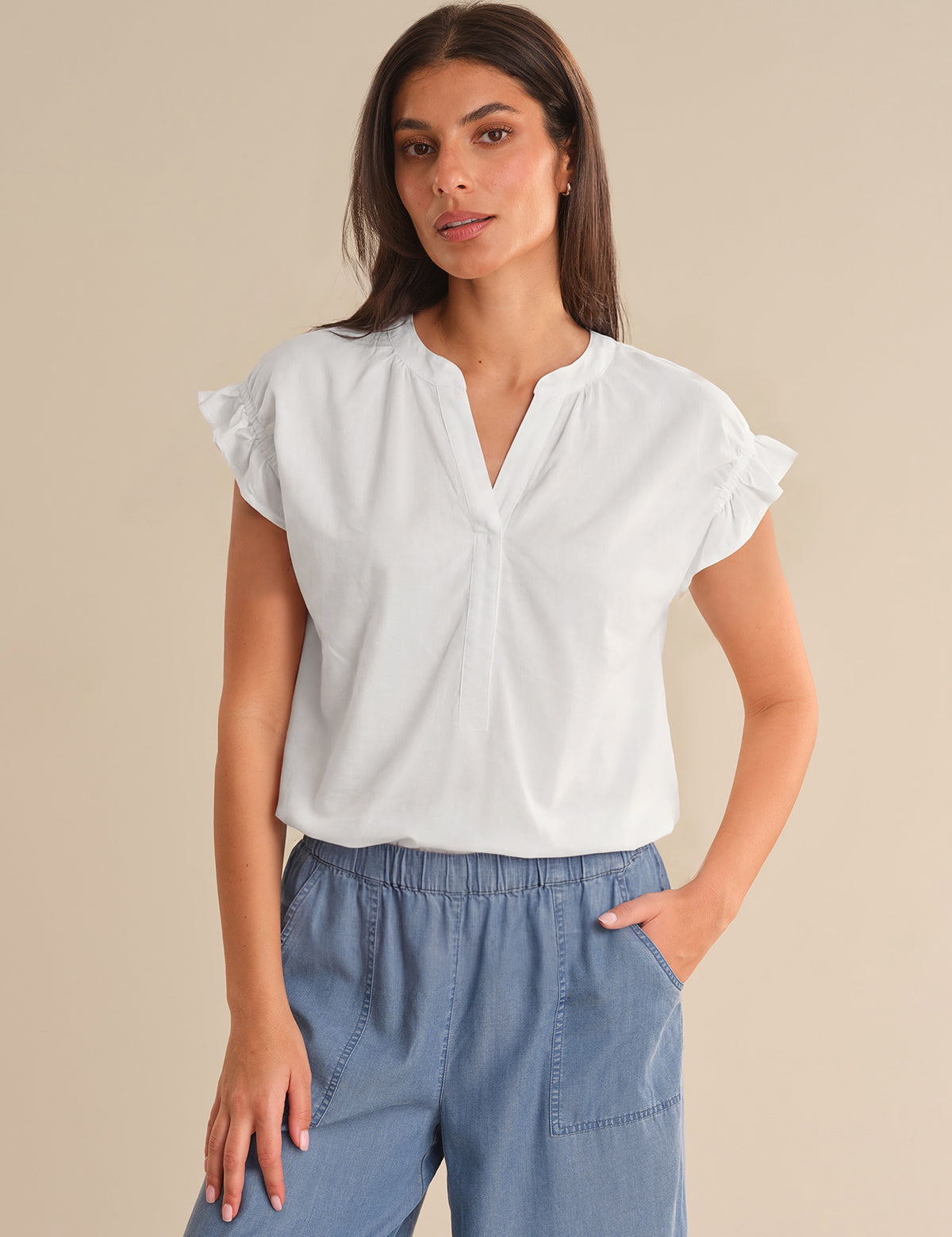 Woman wearing a white blouse with ruffled sleeves and blue pants on a beige background