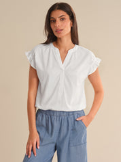 Woman wearing a white blouse with ruffled sleeves and blue pants on a beige background