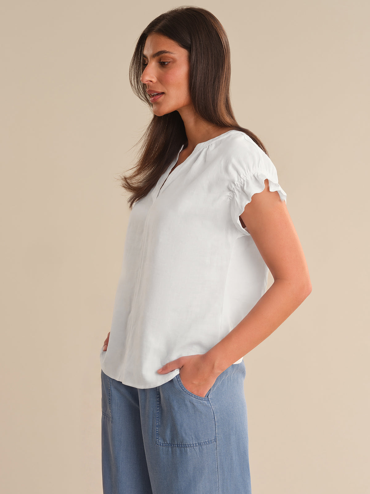Woman wearing a white blouse and blue pants against a beige background