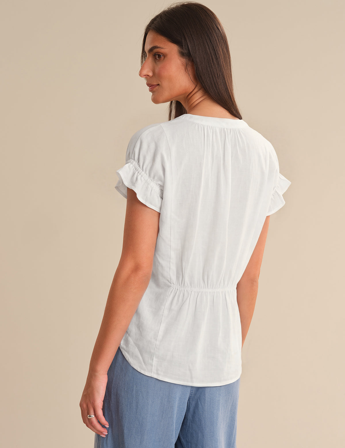 Woman wearing a white blouse with ruffled sleeves on a beige background